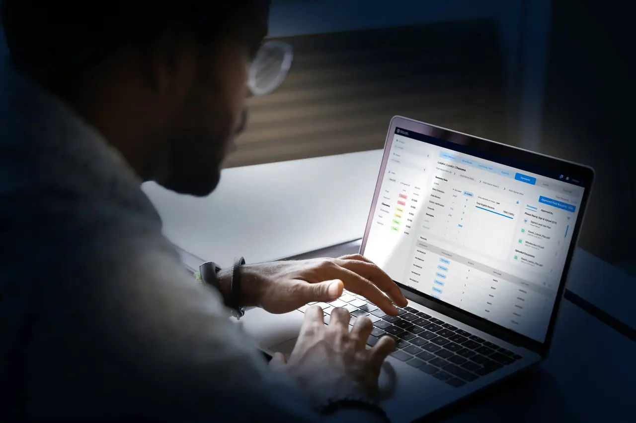 A GIS technician working through records on a laptop in a darkened office