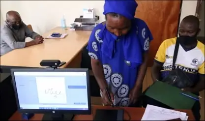 A woman signs on a screen at a records desk while an officer works at a terminal beside her