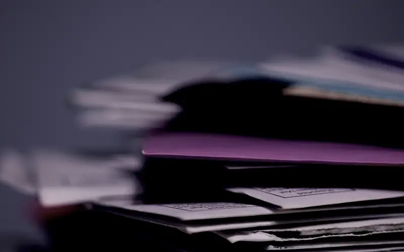 A deep stack of paper land files and folders, the record system a paperless transfer replaces